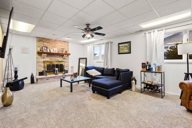 carpeted living room featuring ceiling fan, a paneled ceiling, and a brick fireplace