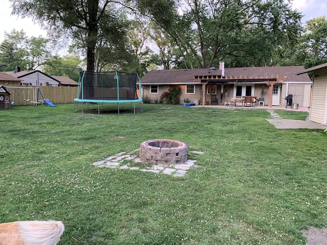 view of yard with a trampoline, a fire pit, a patio, and a playground