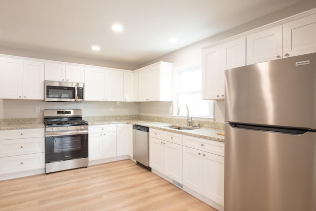 kitchen featuring stainless steel appliances, light stone countertops, sink, and white cabinets