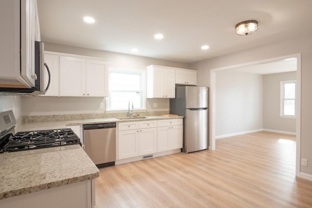 kitchen featuring sink, light wood-type flooring, appliances with stainless steel finishes, light stone countertops, and white cabinets