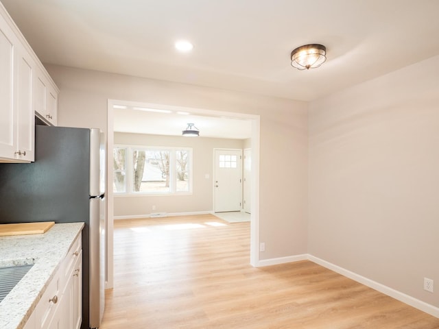 kitchen featuring white cabinetry, light stone countertops, stainless steel fridge, and light hardwood / wood-style floors