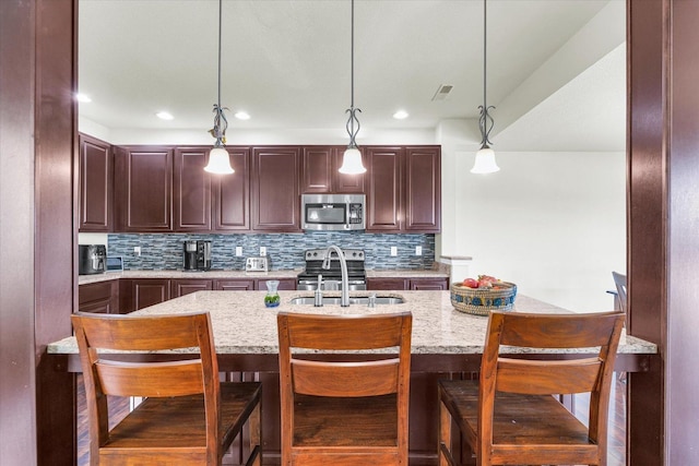 kitchen with decorative backsplash, light stone counters, appliances with stainless steel finishes, pendant lighting, and a sink