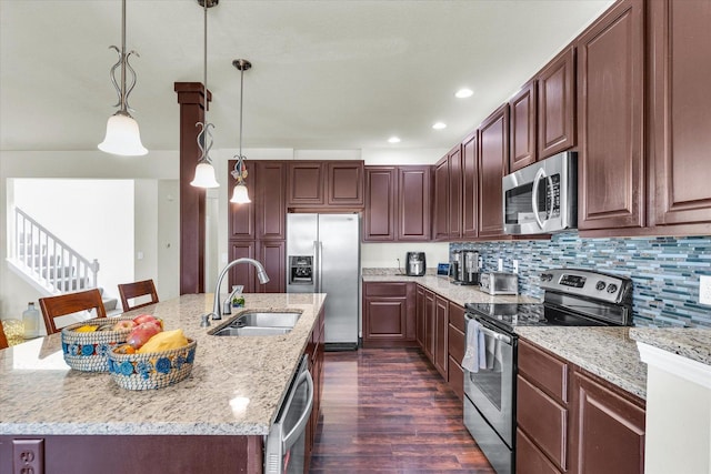 kitchen featuring light stone counters, pendant lighting, a center island with sink, stainless steel appliances, and a sink