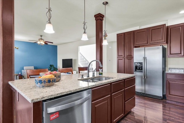 kitchen featuring light stone counters, stainless steel appliances, hanging light fixtures, a sink, and an island with sink