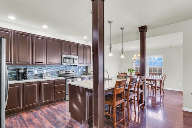 kitchen with a breakfast bar area, stainless steel appliances, dark wood-type flooring, tasteful backsplash, and pendant lighting