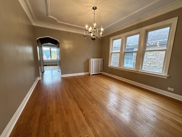 unfurnished dining area with radiator, wood-type flooring, ornamental molding, and a chandelier