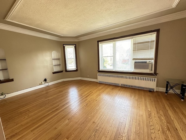 empty room with radiator heating unit, wood-type flooring, cooling unit, ornamental molding, and a textured ceiling