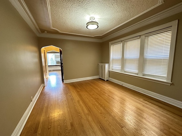 empty room with crown molding, a healthy amount of sunlight, a textured ceiling, and light hardwood / wood-style flooring