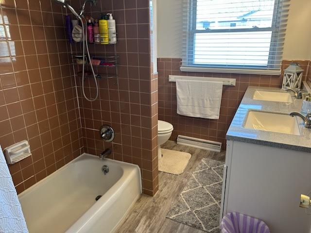 full bathroom with hardwood / wood-style flooring, tile walls, shower / tub combo, vanity, and toilet