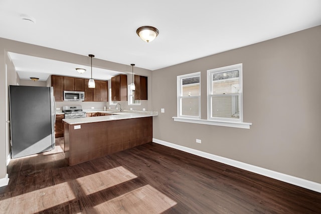 kitchen featuring pendant lighting, sink, dark wood-type flooring, stainless steel appliances, and kitchen peninsula