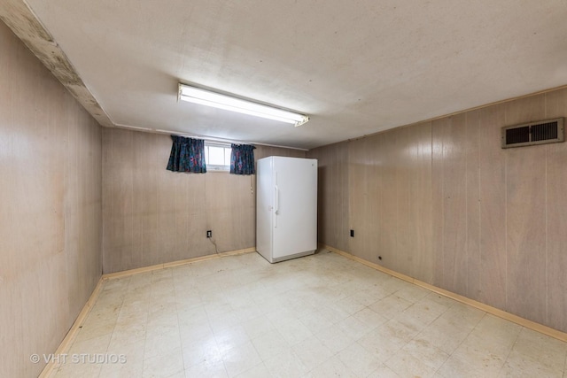 basement featuring wooden walls and white refrigerator