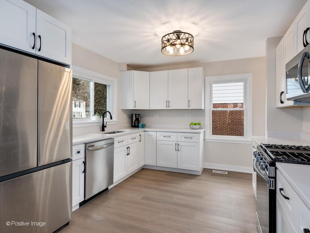 kitchen with white cabinetry, stainless steel appliances, sink, and light wood-type flooring