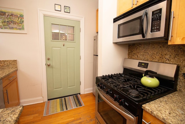 kitchen featuring tasteful backsplash, light stone countertops, light hardwood / wood-style flooring, and stainless steel appliances