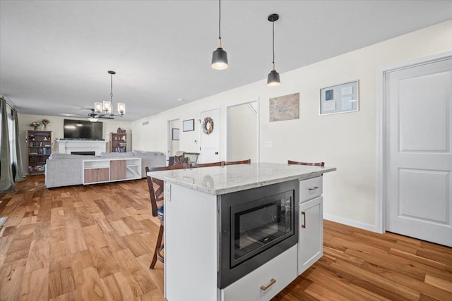 kitchen featuring hanging light fixtures, black microwave, a kitchen breakfast bar, a kitchen island, and light hardwood / wood-style floors