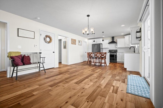 kitchen with wall chimney exhaust hood, decorative light fixtures, light wood-type flooring, stainless steel appliances, and white cabinets