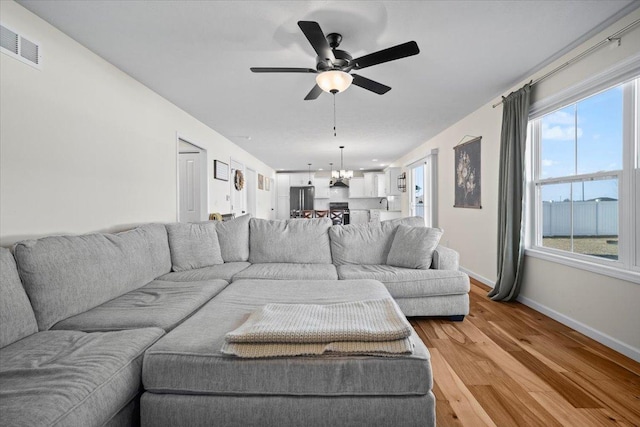 living room with ceiling fan with notable chandelier and light hardwood / wood-style flooring