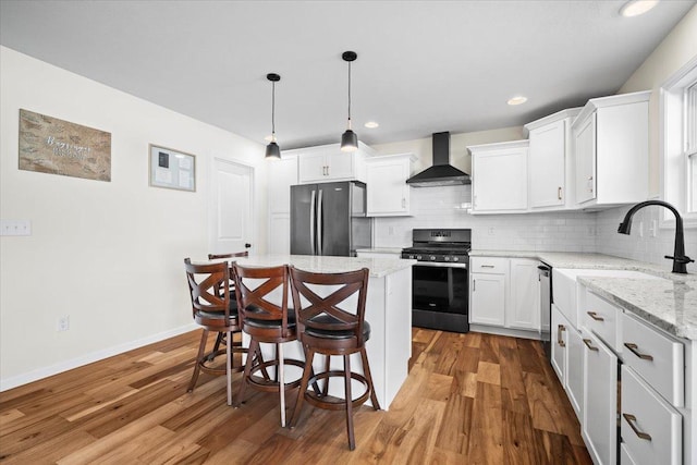 kitchen featuring wall chimney range hood, hanging light fixtures, stainless steel appliances, a center island, and white cabinets