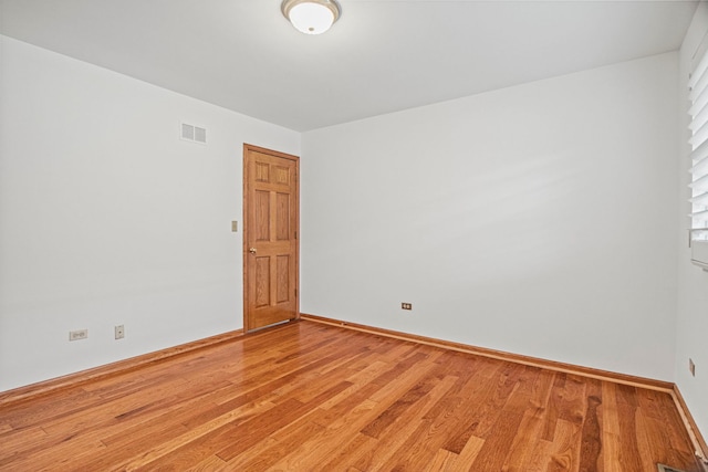 empty room with light wood-style floors, visible vents, and baseboards