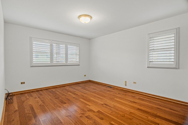 spare room featuring wood-type flooring, visible vents, and baseboards