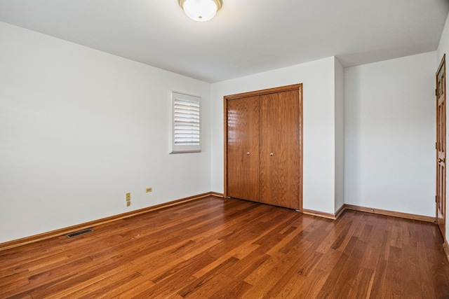 unfurnished bedroom featuring a closet, wood finished floors, visible vents, and baseboards