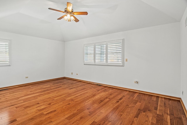 spare room featuring baseboards, visible vents, a ceiling fan, hardwood / wood-style floors, and vaulted ceiling