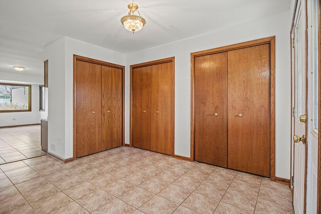 unfurnished bedroom featuring light tile patterned floors, baseboards, and two closets