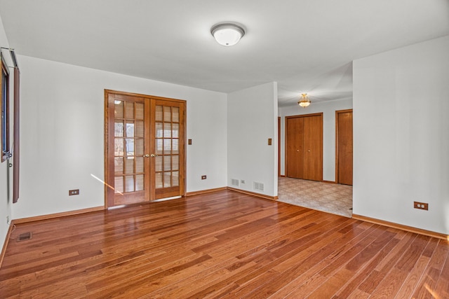 spare room featuring light wood finished floors, french doors, visible vents, and baseboards