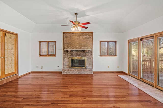 unfurnished living room featuring wood finished floors, a ceiling fan, baseboards, a brick fireplace, and a tray ceiling