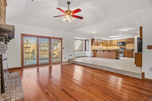 unfurnished living room with light wood-style floors, a tray ceiling, a brick fireplace, and a ceiling fan