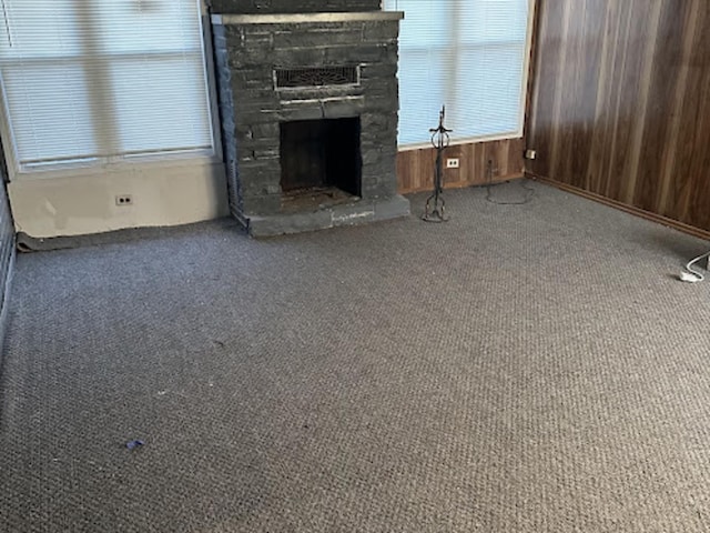 unfurnished living room featuring a stone fireplace, wooden walls, and carpet flooring