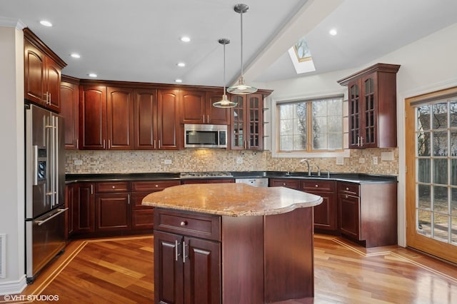 kitchen featuring sink, stainless steel appliances, a kitchen island, decorative light fixtures, and light wood-type flooring