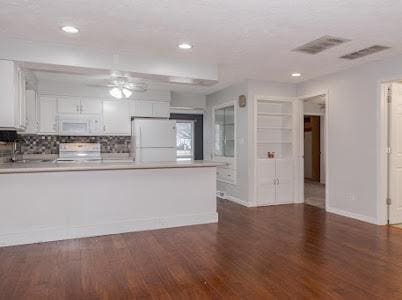 kitchen with dark wood-type flooring, white cabinetry, kitchen peninsula, white appliances, and backsplash