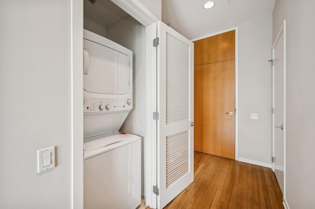 clothes washing area featuring stacked washer and clothes dryer and wood-type flooring