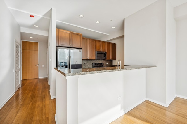 kitchen with backsplash, stainless steel appliances, light hardwood / wood-style floors, stone countertops, and kitchen peninsula