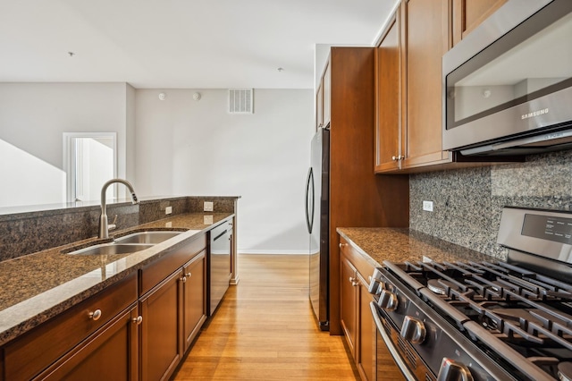 kitchen with sink, tasteful backsplash, dark stone counters, stainless steel appliances, and light hardwood / wood-style floors