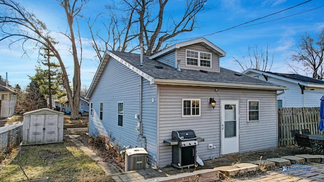 rear view of house with an outbuilding, a shed, roof with shingles, and fence