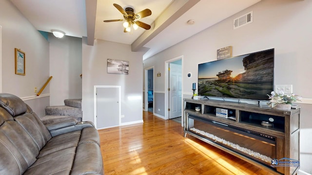 living room featuring visible vents, beamed ceiling, a ceiling fan, light wood finished floors, and stairs