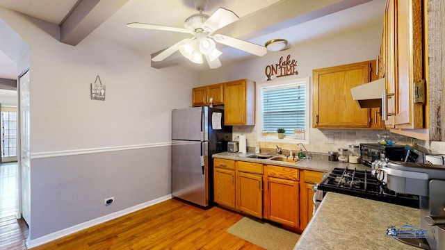 kitchen with a sink, tasteful backsplash, appliances with stainless steel finishes, exhaust hood, and light wood finished floors