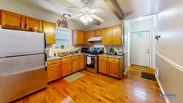 kitchen with under cabinet range hood, a sink, tasteful backsplash, appliances with stainless steel finishes, and light wood finished floors