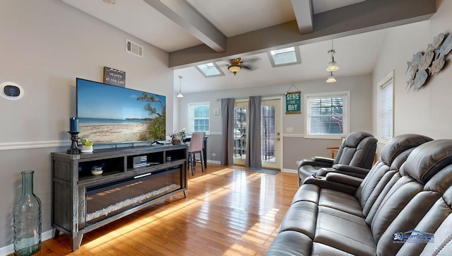 living area with lofted ceiling with skylight, baseboards, visible vents, and light wood-type flooring