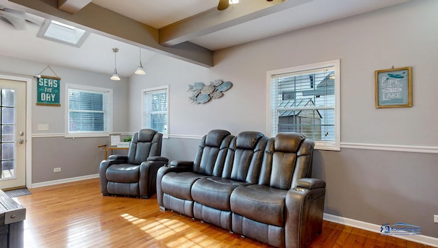 cinema room featuring lofted ceiling with skylight, ceiling fan, baseboards, and wood finished floors