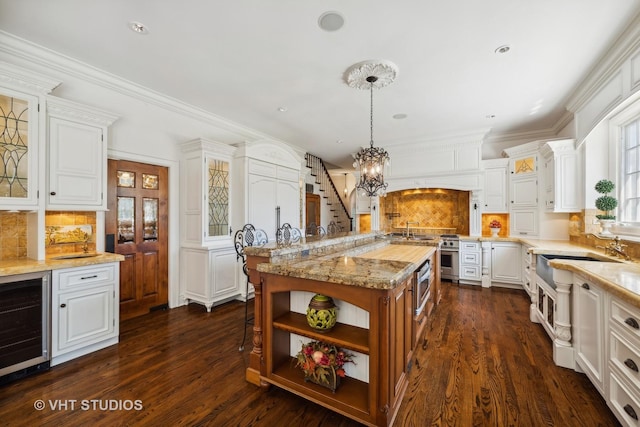 kitchen with pendant lighting, beverage cooler, an island with sink, and white cabinets