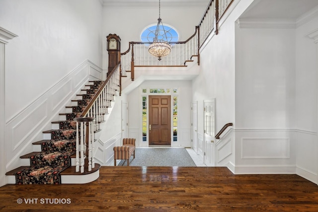 entryway with dark wood-type flooring, a towering ceiling, ornamental molding, and a chandelier