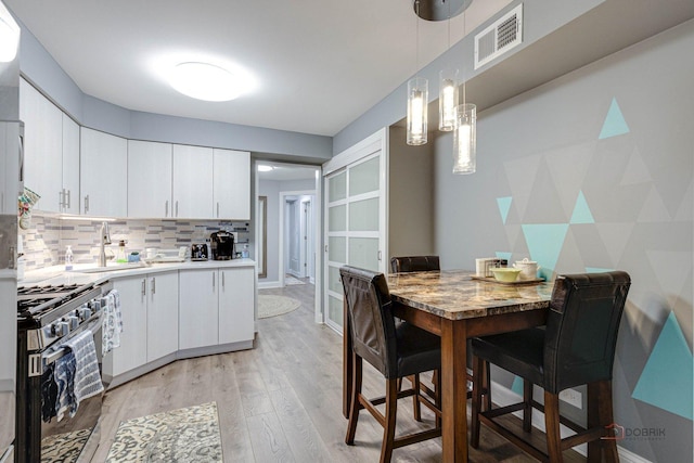 kitchen with white cabinets, decorative backsplash, hanging light fixtures, stainless steel gas range oven, and light wood-type flooring