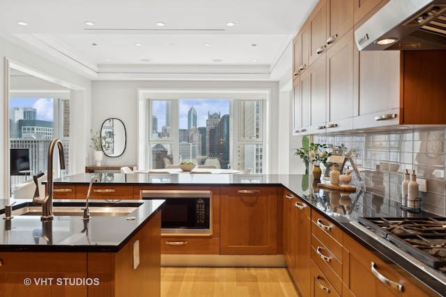 kitchen featuring black microwave, dark stone countertops, backsplash, exhaust hood, and light hardwood / wood-style floors