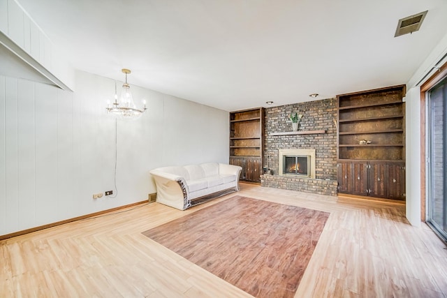 unfurnished living room with built in shelves, a fireplace, a chandelier, and light hardwood / wood-style floors