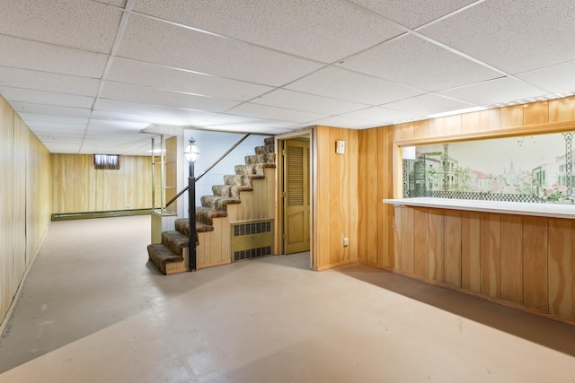 basement with a baseboard radiator, radiator heating unit, wooden walls, and a drop ceiling