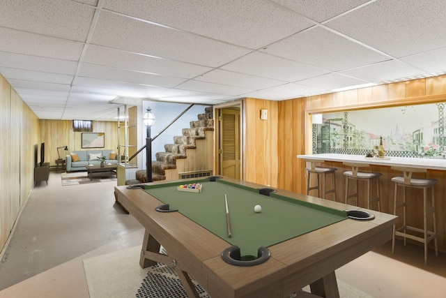 rec room with a paneled ceiling, billiards, wood walls, indoor bar, and concrete floors