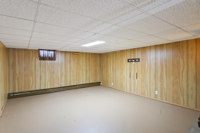 basement with a drop ceiling, a baseboard heating unit, and wooden walls