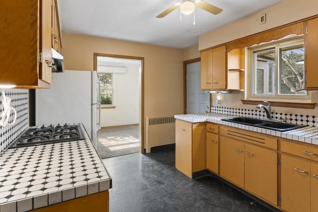 kitchen featuring radiator, sink, ceiling fan, tile countertops, and stainless steel gas stovetop